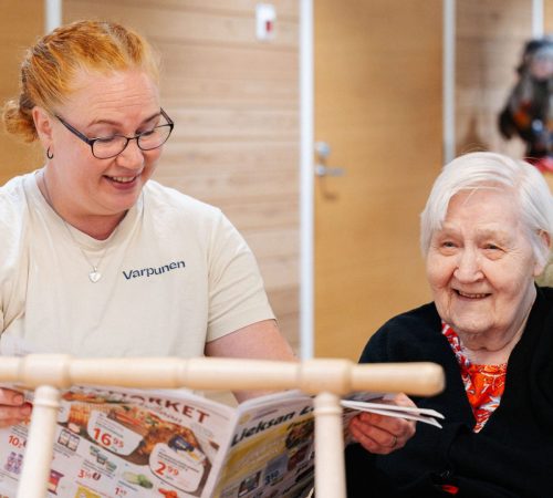 Nuori nainen ja vanha nainen nauravat yhdessä ja katsovat lehteä mukavassa ympäristössä.